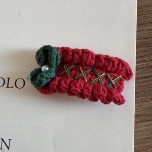 Macro detail of hand-knitted red Christmas hair clip with green bow and white pearl