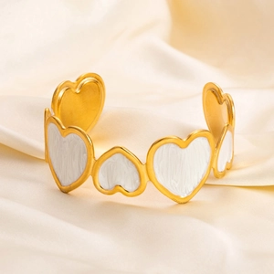 Detail of 18K gold-plated open bangle featuring white enamel heart patterns on satin