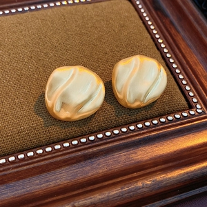 Detailed macro view of gold-tone irregular wavy round earrings with matte brushed finish