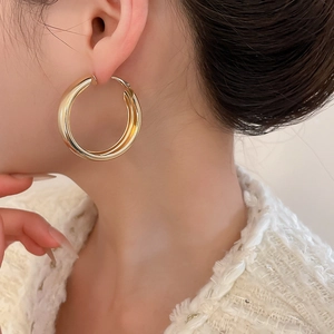 Close-up of a model wearing minimalist large thick gold hoop earrings with glossy finish