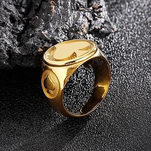 Makroansicht eines goldenen Siegelrings aus Edelstahl mit geprägten Pik-Symbolen auf Stein-Hintergrund