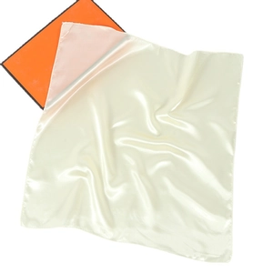 Detail view of a smooth beige silk square scarf draped over an orange box lid