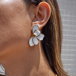Close-up of a white flower earring with gold edges worn by a model for a stylish look