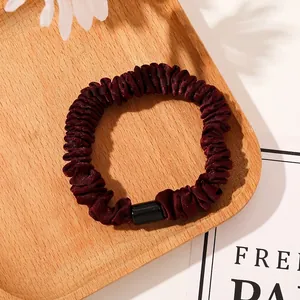 Detail view of burgundy pleated satin hair scrunchie with a sleek black plastic buckle