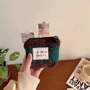 Detail of hand holding mini plush makeup bag with green and brown contrast and zipper