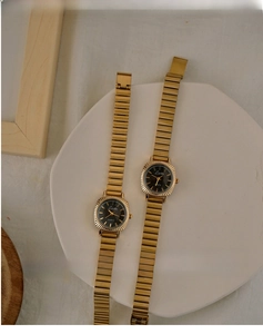 Detail of vintage gold quartz watch with black round dial and metallic elastic strap