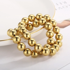 Detailed view of two gold-plated elastic bead bracelets on a white ceramic plate