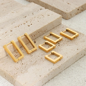 Three sizes of rectangular gold-plated stainless steel earrings on a beige stone surface