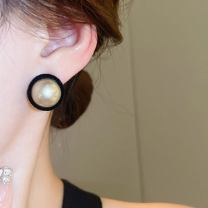 Close-up of velvet-textured black frame round pearl earrings on model's ear