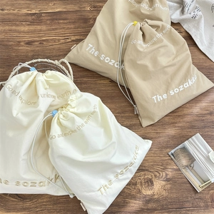 Drawstring travel organizer bags in cream and khaki with embroidery on wood background