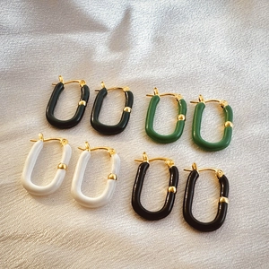 Close-up of U-shaped gold earrings with black, green and white enamel on silk fabric