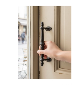 Close-up of vintage black iron cabinet handle with decorative ball ends on a wood door