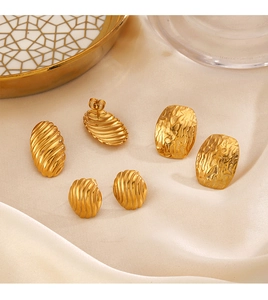 Detail of three pairs of textured gold geometric earrings on elegant beige silk fabric