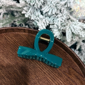 Detail of teal green bow hair claw clip on wooden tray with snowy winter background
