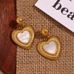 Gros plan de boucles d'oreilles cœur dorées avec nacre sur tissu en lin rustique