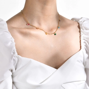 Detail of 18K gold plated necklace with colorful gemstones worn on a female neck
