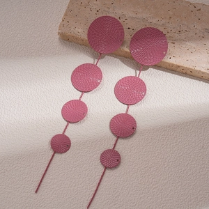 Detail view of pink geometric tiered fringe earrings with textured discs on natural stone