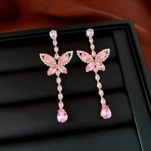 Macro view of luxury pink butterfly earrings with crystal tassels on a black tray