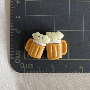 Detailed view of yellow resin cartoon beer mug charms with smiley faces on a cutting mat