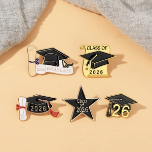 Close-up of 5-piece Class of 2026 graduation enamel pins on beige surface background