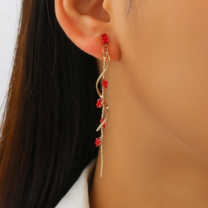 Close-up of gold spiral tassel earrings with red marquise stones worn by a model
