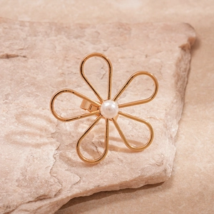 Detailed view of a gold flower ring with center pearl on a natural stone background