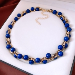 Close-up of vintage gold chain intertwined with blue lapis beads in a white velvet box