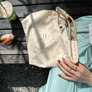 Detail of cartoon canvas tote with braided orange rope handles on a wooden bench
