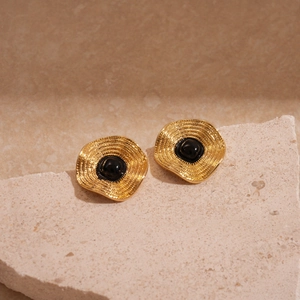 Détail de boucles d'oreilles dorées vintage avec pierre noire sur socle de pierre