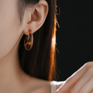 Close-up of leopard resin C-shape hoop earrings on model with warm backlighting