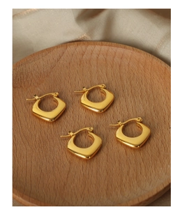 Vier goldene quadratische Creolen auf einem runden Holzteller mit beige Stoff