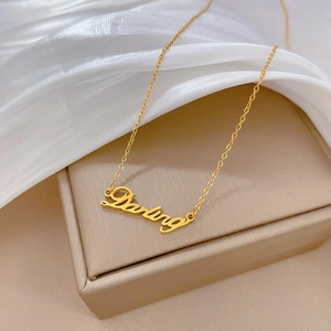 Close-up of golden 'Darling' script pendant necklace on a soft silk background