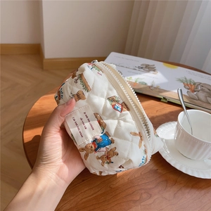 Quilted cream cosmetic bag with cute rabbit pattern held over a rustic wooden table