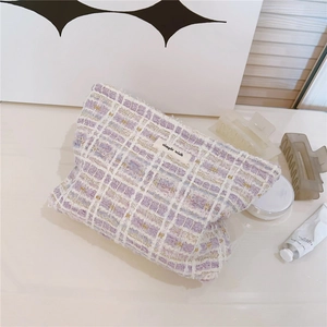 Close-up of purple and white tweed makeup bag featuring gold silk thread and woven label