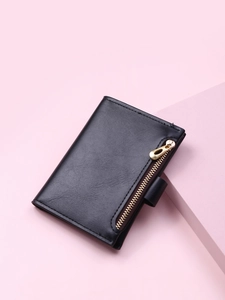 Detail of short black PU leather wallet with gold zipper and snap fastener on pink background