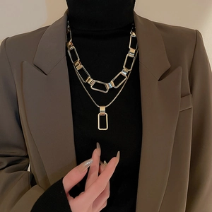 Detail of layered gold chain necklace featuring thick links and square pendant on a model