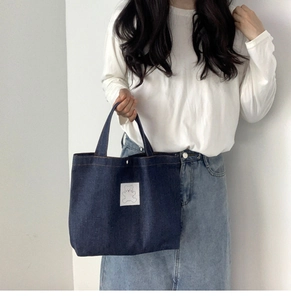 Detailed view of deep blue denim handbag with white bear patch held by a model