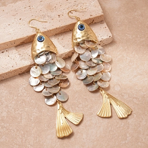 Detailed view of fish-shaped earrings with shell scales and blue eyes on stone texture