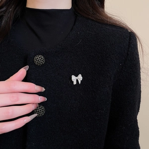 Close-up of sparkling zircon bow brooch pinned on black tweed jacket worn by a model