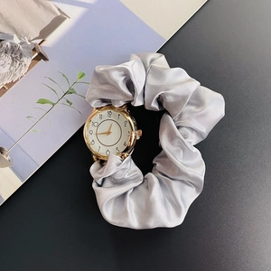 Detail of silver satin scrunchie watch band with golden round dial on dark background