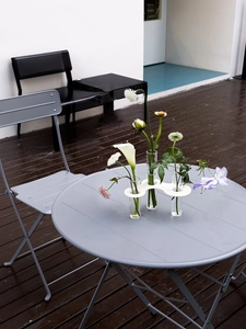 Modern white wave-shaped bud vase holder with three clear glass test tubes on a patio table
