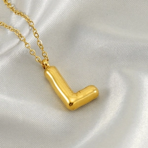 Macro shot of gold puffy balloon letter L pendant on fine chain over white silk fabric