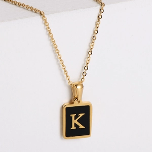 Close-up of gold square pendant with black background and letter K on metal chain