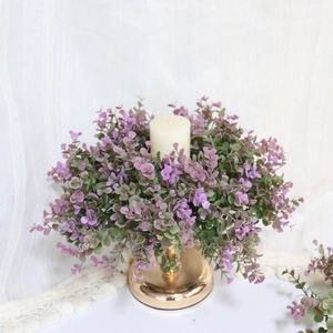 Detail of purple eucalyptus wreath surrounding a cream candle on a gold metal base