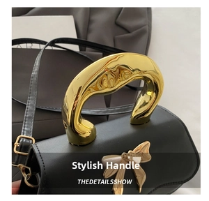 Detail of black leather handbag featuring bold gold metal handle and butterfly buckle