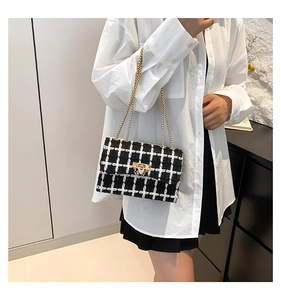 Close-up of black and white tweed crossbody bag with golden chain strap and lock detail