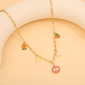Close-up of golden stainless steel necklace with strawberry and heart pendants on beige stand