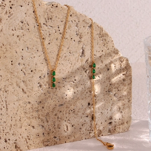Close-up of gold necklaces with three green teardrop stones on a beige stone