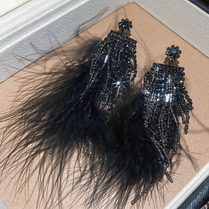 Détail de boucles d'oreilles en plumes noires avec fleurs en strass et pompons de perles en boîte