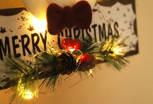 Detail eines Weihnachtskranzes mit Zapfen, Beeren, LED-Lichtern und Merry Christmas Schild